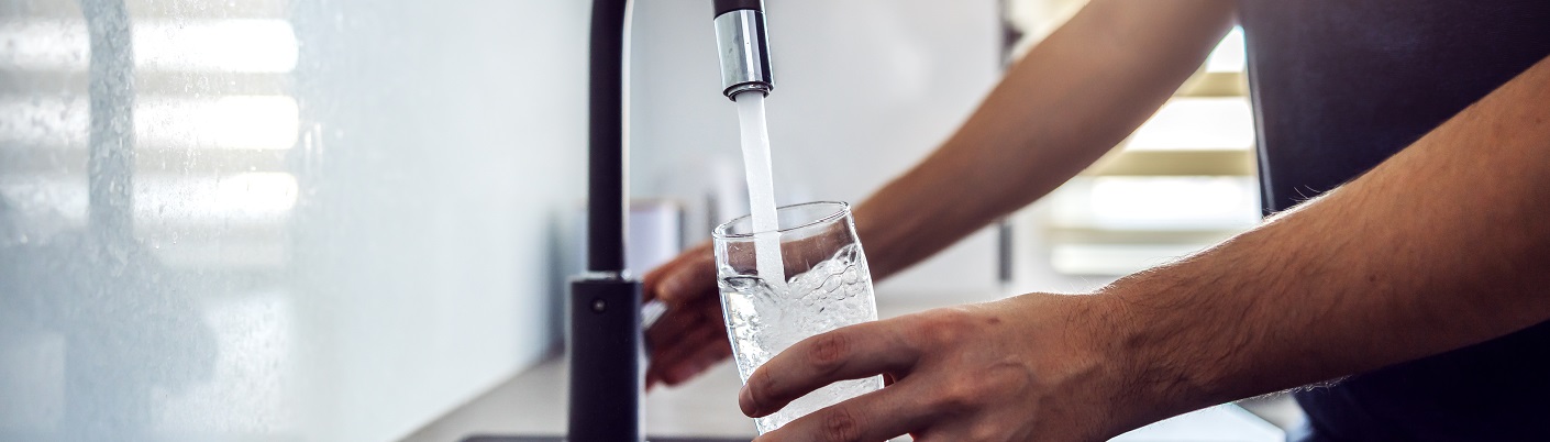 Person pouring water into a glass from a kitchen tap